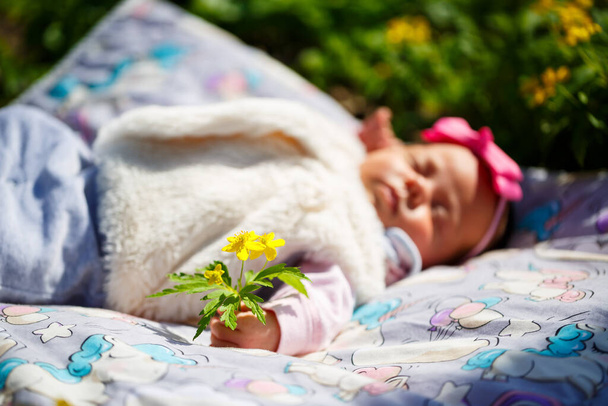 Gros plan bébé avec un arc sur la tête repose sur un plaid blanc sur l'herbe verte. Le printemps est dans la rue, le soleil brille sur l'enfant - Photo, image