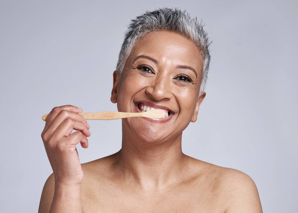 Mature woman, toothbrush and brushing teeth on studio background, morning grooming routine or healthcare wellness. Portrait, smile or beauty model in dental care cleaning or happy hygiene maintenance. - Foto, Bild