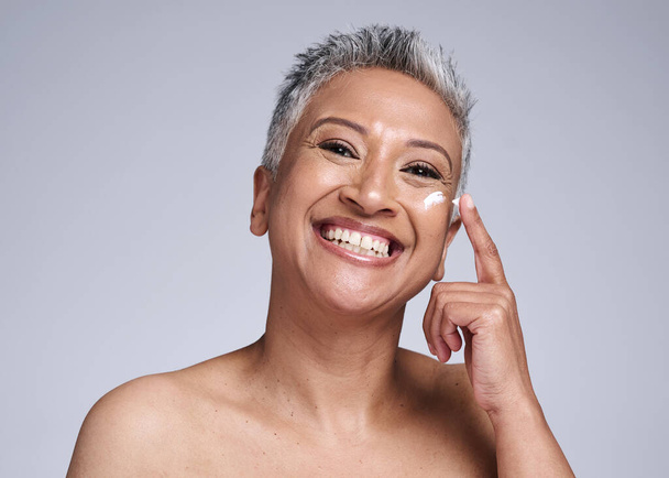 Skincare, facial cream and senior black woman isolated on gray background in studio for spa. Beauty, wellness and portrait of old woman apply lotion, sunscreen or anti aging beauty products to face. - Foto, Imagem