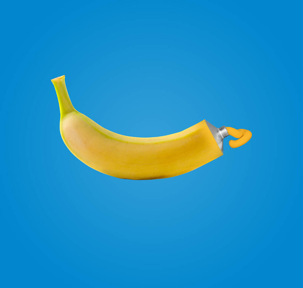 Κολάζ σύγχρονης τέχνης. Μια μπανάνα και μια κίτρινη μπογιά. Φωτογραφία σε μπλε φόντο το καλοκαίρι. Σύγχρονη έννοια τροφίμων. - Φωτογραφία, εικόνα