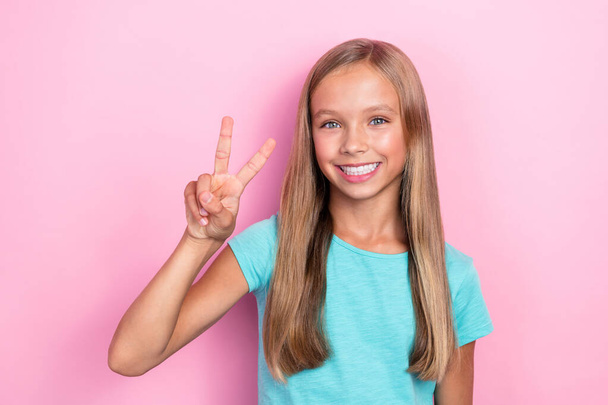 Closeup photo of little nice young preteen schoolgirl wear cyan t-shirt toothy smiling showing v-sign enjoy learning isolated on pastel pink color background. - Foto, imagen