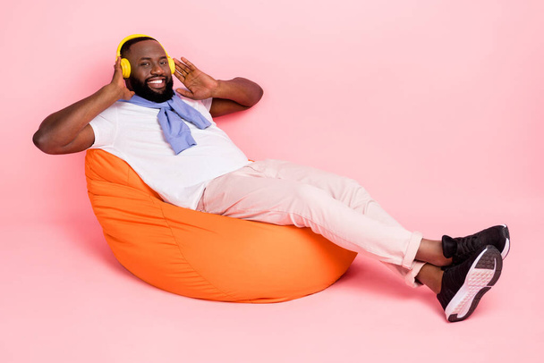 Teljes test fotó fiatal srác pihentető babzsák hallgatni kedvenc zenei műfaj headset elszigetelt rózsaszín színű háttér. - Fotó, kép
