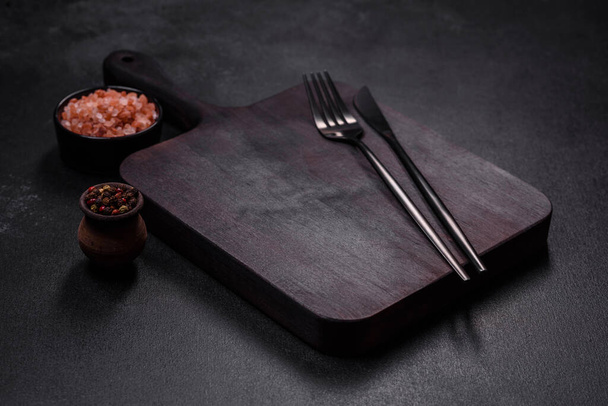 Placa de corte de madeira com utensílios de cozinha em um fundo de concreto preto. Cozinhar em casa - Foto, Imagem