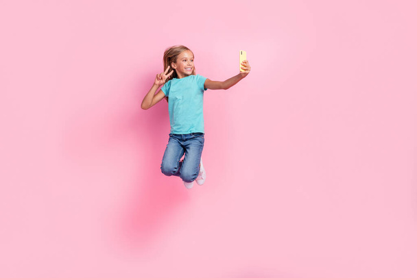 Full length photo of adorable cute small kid wear turquoise t-shirt jumping high recording video vlog v-sign isolated pink color background. - Foto, Imagen