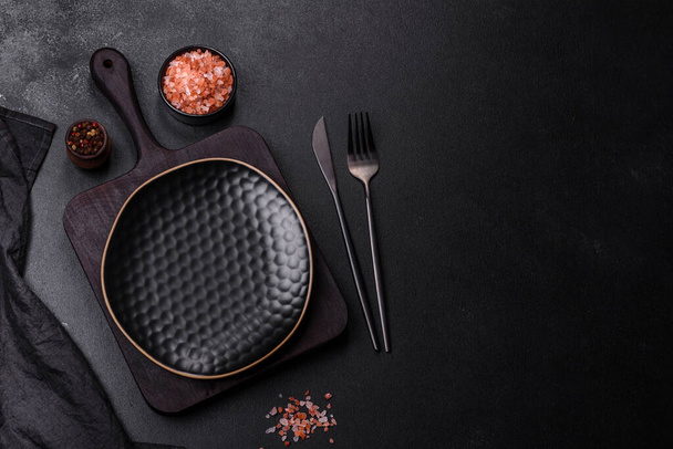 Schwarzer leerer Teller, Besteck und Serviette auf einer steinernen Tischplatte. Tisch gedeckt - Foto, Bild