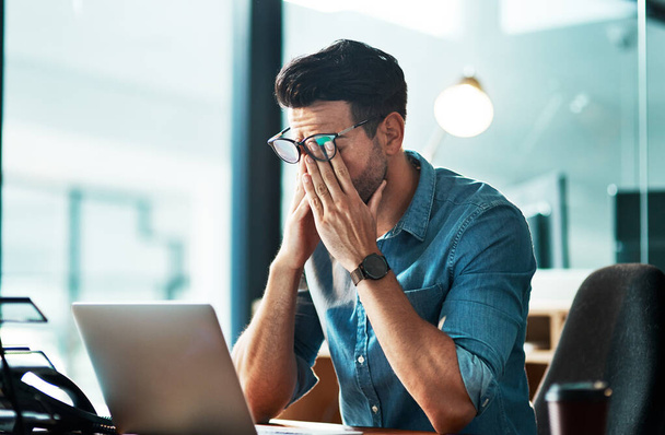Te moe om er om te geven. een jonge zakenman die stress ervaart tijdens het gebruik van een laptop in een modern kantoor - Foto, afbeelding
