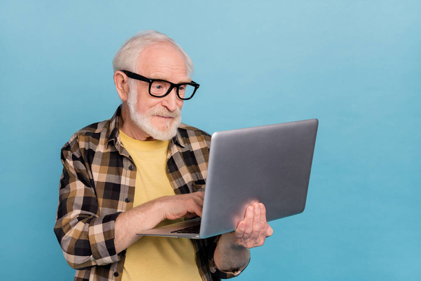 Photo of attractive cute retired man wear plaid shirt spectacles working modern device isolated blue color background. - 写真・画像