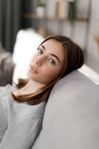 Ritratto di donna caucasica rilassata con capelli castani che si rilassa da sola sul comodo divano di casa. Concetto di persone, tempo libero e stili di vita. - Foto, immagini