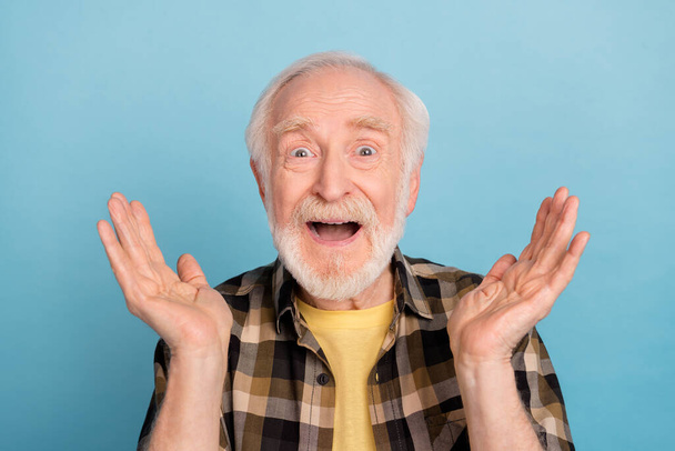 Photo of funny excited retired man wear plaid shirt open mouth rising arms isolated blue color background. - Fotografie, Obrázek