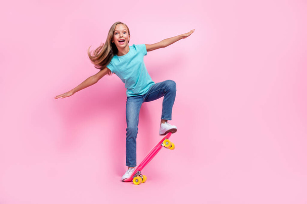 Full length photo of sweet excited small kid wear turquoise t-shirt riding skateboard empty space isolated pink color background. - Foto, Bild