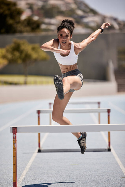 Γυμναστική, εμπόδια και αθλητής άλμα σε τροχιά σε ένα υπαίθριο στάδιο για άσκηση καρδιο. Αθλητισμός, τρέξιμο και γυναίκες που αθλούνται στο γήπεδο για προπόνηση και άσκηση με ενέργεια, κίνητρο και ταχύτητα - Φωτογραφία, εικόνα