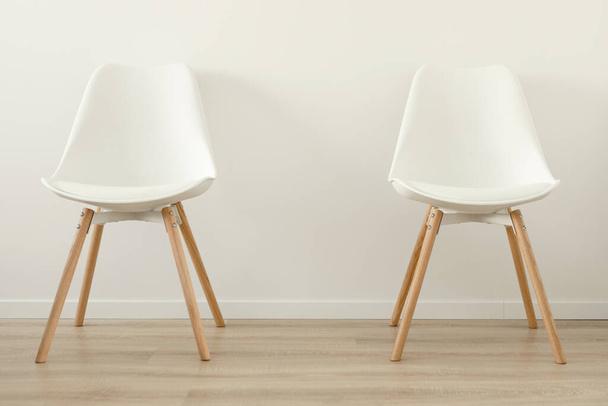 İki boş beyaz sandalye, ofis ya da odada beyaz bir duvara karşı birbirinden uzaktır. Yüksek kalite fotoğraf - Fotoğraf, Görsel