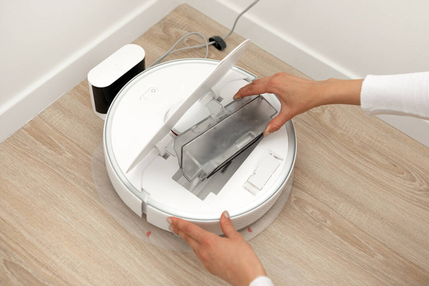 The girl cleans the robot vacuum cleaner, takes out a box with garbage. High quality photo - Zdjęcie, obraz