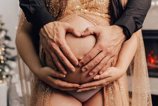 Muž a žena drží kulaté břicho s dítětem uvnitř. Těhotná dvojice čeká na dítě. Manžel se dotkl rukou své ženy. Očekávám novorozeně dítě. Budoucí rodina - Fotografie, Obrázek