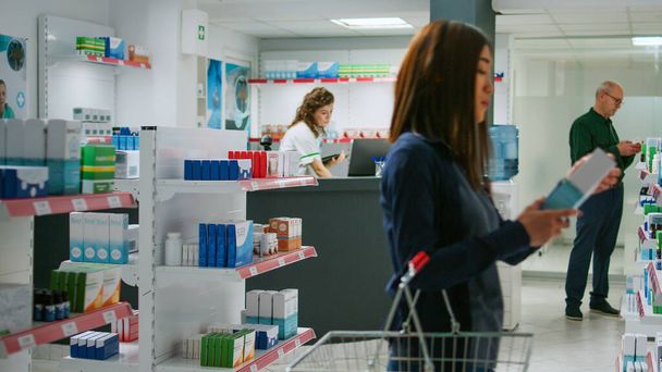 Monietninen ryhmä asiakkaita, jotka tarkastelevat lääkkeitä apteekkien hyllyillä, tarkistavat lääkkeitä ja laatikoita, joissa on vitamiineja tai pillereitä. Asiakkaat etsivät täydentää. - Valokuva, kuva
