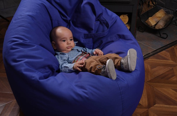 Little infant boy sitting on a blue bean bag with copy space - Photo, Image
