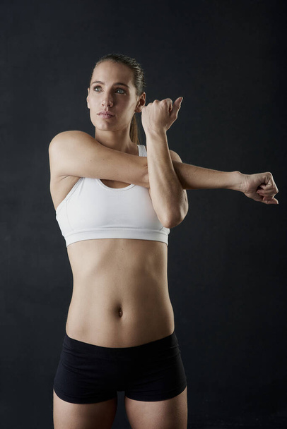 She knows how important stretching is. Studio shot of an attractive young woman warming up against a dark background - Photo, Image