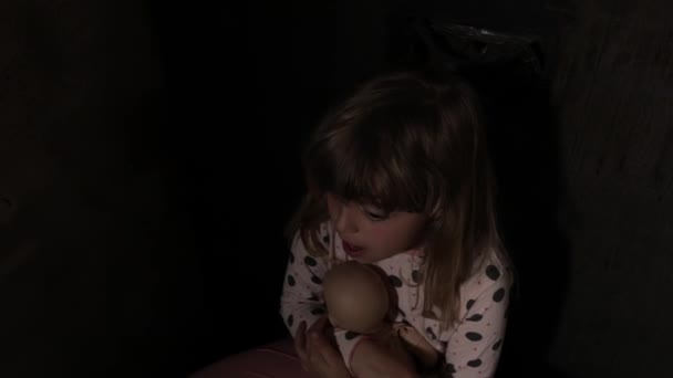 Menina assustada com uma boneca em um quarto escuro. Imagens 4k de alta qualidade - Filmagem, Vídeo
