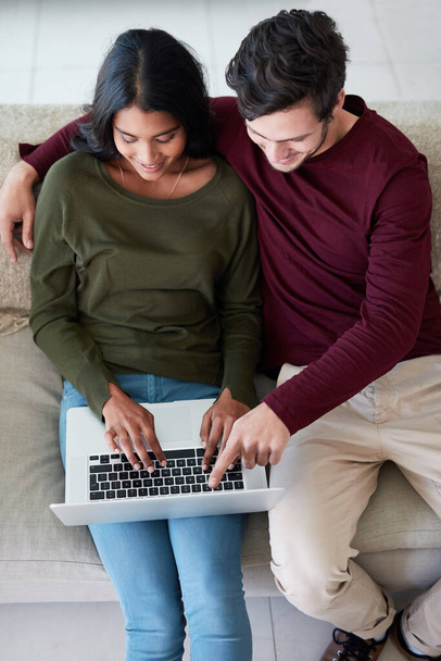 Verbinding maken tijdens het bloggen. een aanhankelijk jong echtpaar met behulp van hun laptop tijdens het zitten op de bank thuis - Foto, afbeelding