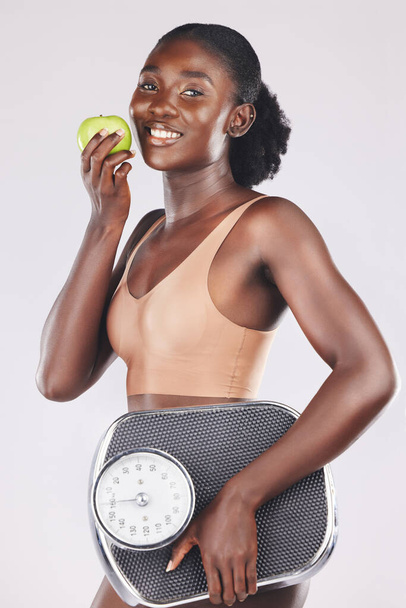 Apple, scale and weightloss with a black woman in studio on a gray background to promote healthy eating or diet. Food, fruit and exercise with an attractive young female posing for natural vitamins. - Foto, Imagem
