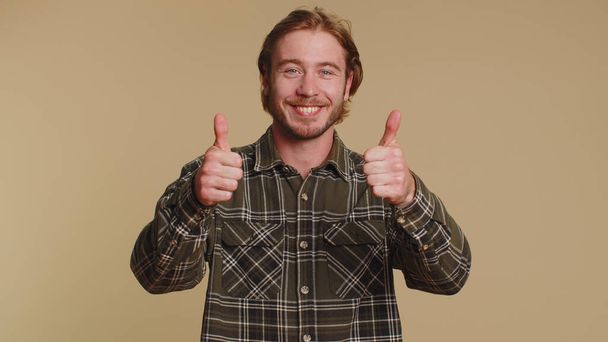 Όπως. Γενειοφόρος ξανθός άντρας με καρό πουκάμισο σηκώνει το δάχτυλο συμφωνεί με κάτι ή δίνει θετική απάντηση συνιστά διαφήμιση αρέσει καλό. Νεαρός απομονωμένος σε μπεζ φόντο στούντιο - Φωτογραφία, εικόνα
