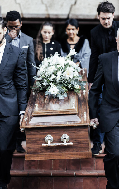 Death, funeral and people with coffin to cemetery, graveyard and morgue for burying, cremation or ritual. RIP, mourning and burial of dead in casket at church ceremony, respect and christian religion. - Photo, Image