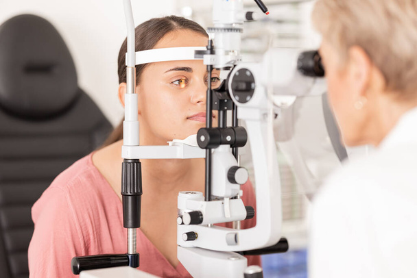 Examen oculaire, optométriste et ophtalmologiste bureau avec machine optique pour examiner la vision iris faible, pupille ou lentille du globe oculaire. Femme, test clinique optique et test professionnel de soins oculaires opticien. - Photo, image