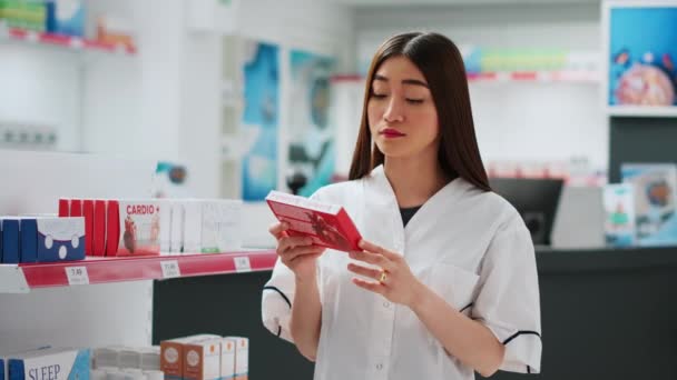 Asian employee working in pharmaceutical drugstore shop, looking at cardiology medicaments. Analyzing medical treatment and supplements in pharmacy retail store, healthcare. Handheld shot. - Footage, Video