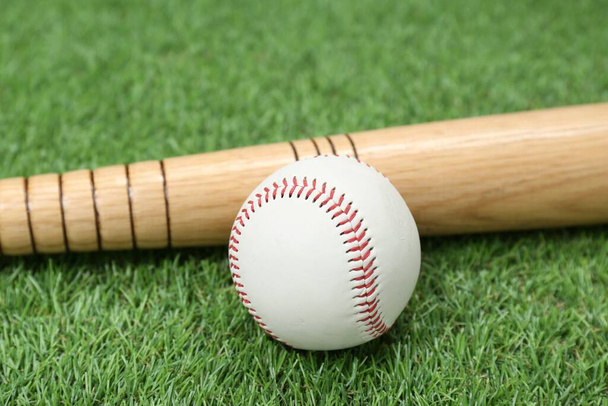 Wooden baseball bat and ball on green grass, closeup. Sports equipment - Foto, Imagem