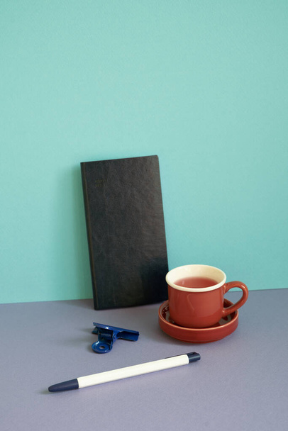 Notebook, pen, clip, cup of tea on purple desk. blue background. workspace - Photo, Image