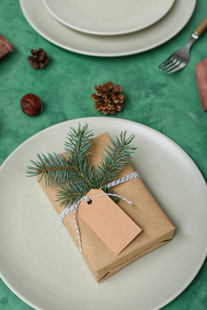 Красивая сервировка стола с рождественским подарком, еловыми ветвями и конусами на зеленом фоне, крупным планом - Фото, изображение