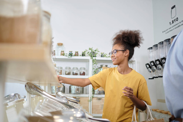 Young African American woman is choosing and shopping for organic products in refill store with reusable bag, zero-waste grocery, and plastic-free, eco environment-friendly, sustainable lifestyles. - Foto, immagini
