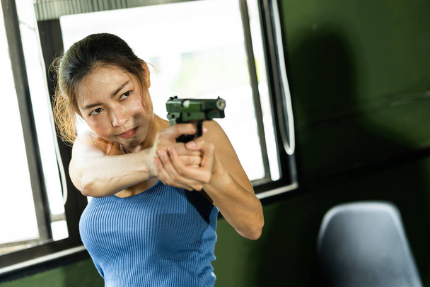 Beautiful young asian serious woman holding gun and getting ready for the attack. Woman aiming a gun, focus on the gun. - Photo, Image
