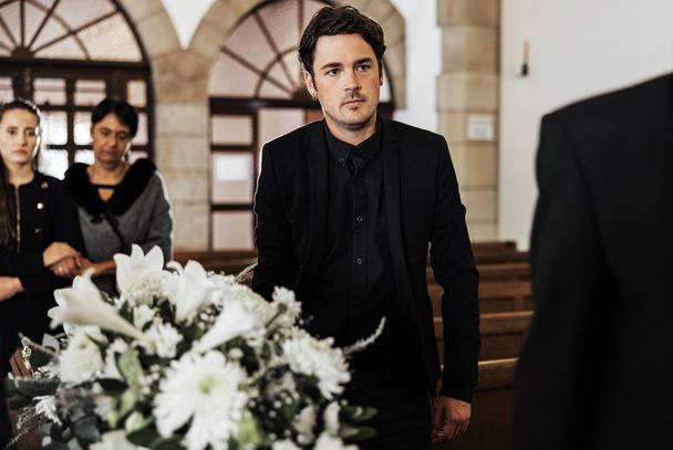Begrafenis, dood en verdriet met een man die een doodskist droeg in een kerk tijdens een ceremonie. Bloemen, pak en verlies met een man die een kist vasthoudt terwijl hij door een kapel loopt om te rouwen. - Foto, afbeelding