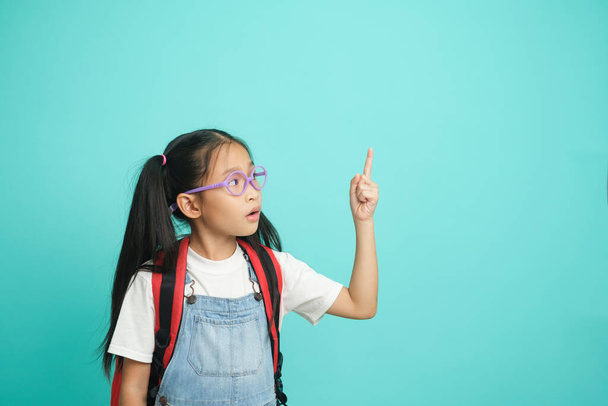 Close-up kid schoolgirl Pointing Fingers At Copy Space, she nice cute attractive cheerful amazed. isolated on blue pastel background. Educational concept for school - Photo, image
