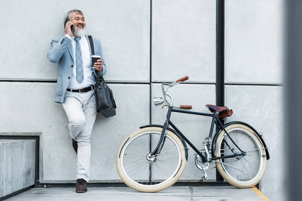 Bicycle, phone call and business man in city for communication, networking and carbon footprint travel marketing update with smile. Happy, healthy senior corporate manager coffee, bike and cellphone. - Photo, Image