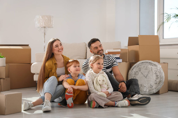 Happy family sitting on floor in new apartment. Moving day - 写真・画像
