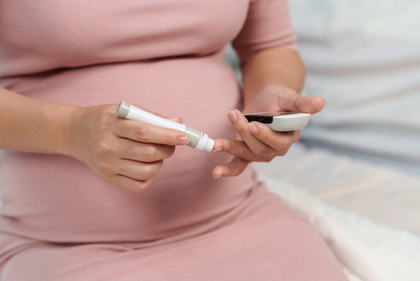 close up of pregnant woman holding glucose meter and checking blood sugar level by herself at home. gestational diabetes concept. - Φωτογραφία, εικόνα