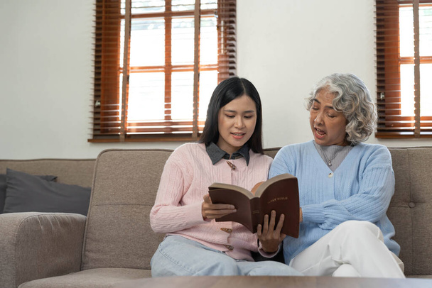 Frau liest ein Buch, während sie mit der glücklichen Großmutter zu Hause sitzt. - Foto, Bild