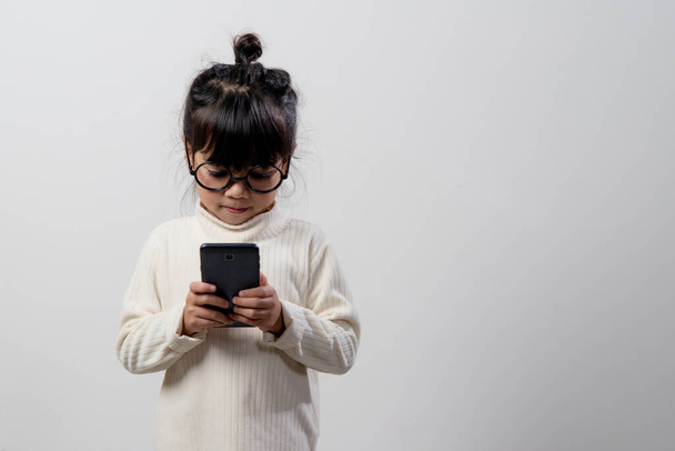 Petite fille asiatique utilisant un téléphone en gros plan, distrait d'étudier, assis à une table avec des cahiers, un joli enfant qui s'amuse avec un smartphone, regarder le webinaire, faire des études à domicile - Photo, image
