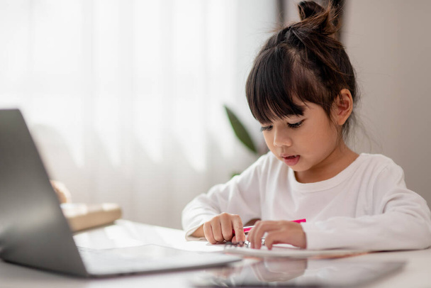 Asian schoolgirl doing her homework with laptop at home. Children use gadgets to study. Education and distance learning for kids. Homeschooling during quarantine. Stay at home - Fotoğraf, Görsel