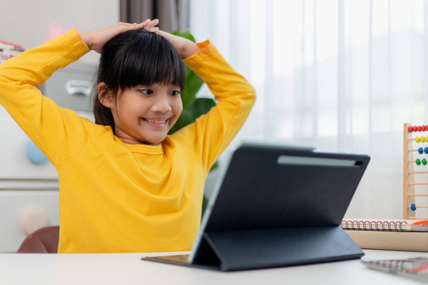 Aziatisch schoolmeisje doet haar huiswerk met digitale tablet thuis. Kinderen gebruiken gadgets om te studeren. Onderwijs en afstandsonderwijs voor kinderen. Thuisonderwijs tijdens de quarantaine. Blijf thuis. - Foto, afbeelding