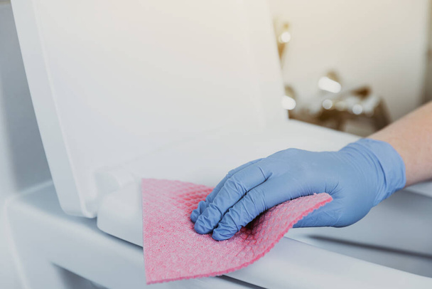Close up on woman hand gloved in blue rubber protective gloves. Housewife cleaning toilet bowl, seat with detergent liquid, wet wipe in bathroom, restroom. Female washing, disinfecting toilet seat - Photo, image