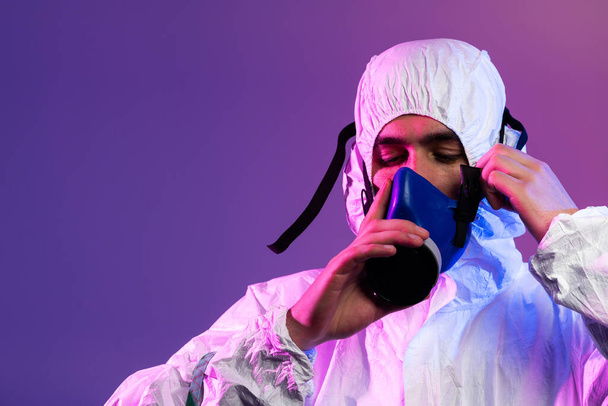 Coronavirus covid-19 pandemic. Doctor scientist wearing protective biological suit and mask due to global healthcare epidemic warning and danger background in blue and pink neon lights background - Φωτογραφία, εικόνα