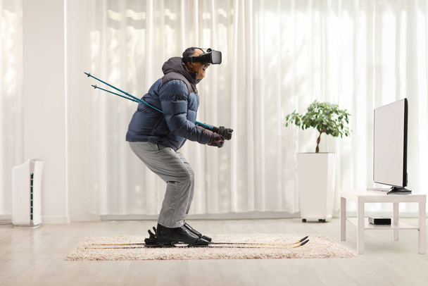 Full length profile shot of a mature man skiing with vr headset on a carpet at home - Photo, image