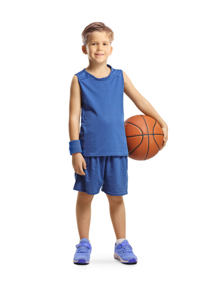 Full length portrait of a boy in a blue sports jersey holding a basketball and smiling at camera isolated on white background - Foto, immagini