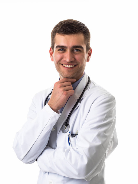 Portrait of hero in a white coat. Cheerful smiling young doctor with a stethoscope in a medical hospital standing against a white background. Coronavirus covid-19 danger alert. High quality photo - Photo, image