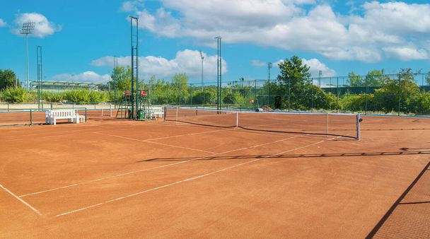 Baseline and net of an empty clay tennis court on a sunny day - Valokuva, kuva