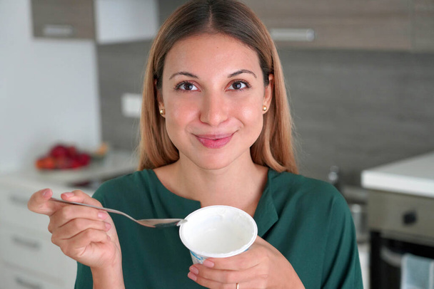 Attractive woman holds bowl of Greek yogurt in her hand and smiles at camera indoors - 写真・画像