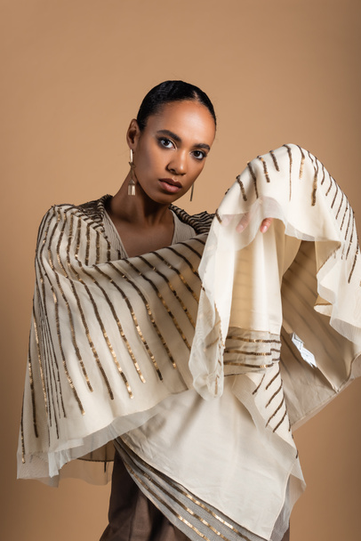 rich african american woman in golden accessories posing with shawl isolated on beige - Photo, Image